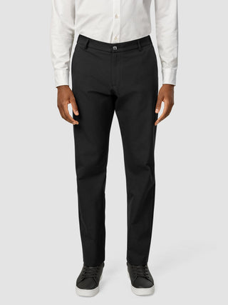 En mann kledd i en hvit skjorte med knapper, Essential Pants Relaxed Fit Black og svarte joggesko.