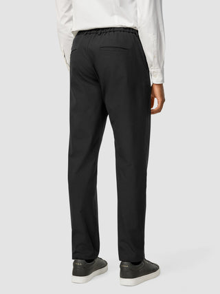Bakfra-bilde av en person som har på seg svarte Essential Pants Relaxed Fit og Arkk-joggesko.