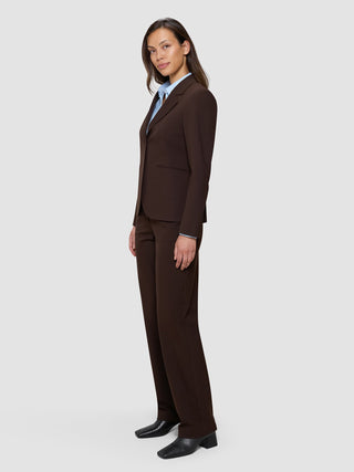 En kvinne i en «Women’s Essential Fitted Blazer» i fargen «Espresso» og matchende bukser, sammen med en lyseblå skjorte med krage.