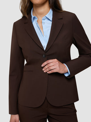 En kvinne som har på seg en «Women’s Essential Fitted Blazer» i fargen «Espresso» over en lyseblå skjorte med knapper.