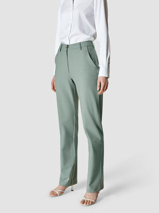 En person i en hvit skjorte med knapper og Essential Pants Straight Calm Green Melange, med hvite sandaler med hæl.