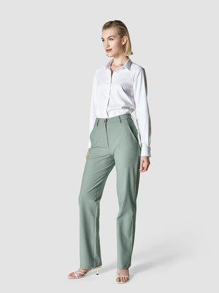 En kvinne kledd i en hvit skjorte med knapper og Essential Pants Straight i fargen Calm Green Melange.