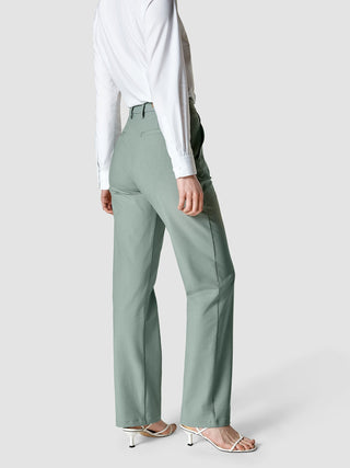 En person sett bakfra, kledd i en hvit langermet skjorte, «Essential Pants Straight Calm Green Melange» og sandaler.