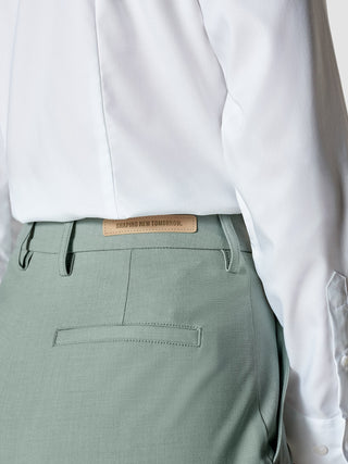 En hvit skjorte stappet inn i Essential Pants Straight Calm Green Melange med et SHAPING NEW TOMORROW-lærmerke.