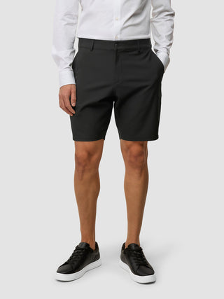 En person i en hvit skjorte med knapper og Essential Shorts Black, med svarte joggesko.