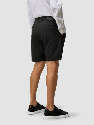 En person sett bakfra, kledd i en hvit skjorte og svarte Essential Shorts, samt svarte joggesko.