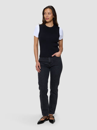 En kvinne som har på seg en svart, finstrikket ribbvest for kvinner over en hvit T-skjorte, mørke jeans og svarte ballerinasko.