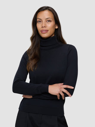 En kvinne iført en svart, finstrikket turtleneck, med armene i kors.