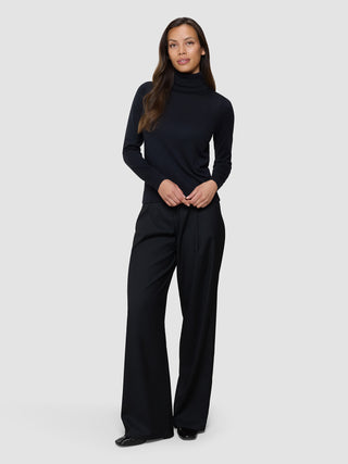 En kvinne kledd i en svart, fint strikket turtleneck og svarte bukser i skandinavisk design.