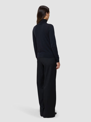 En kvinne sett bakfra, kledd i en svart, finstrikket turtleneck og svarte bukser i skandinavisk design.