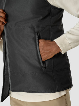 En person som har på seg en svart Utility Vest over en hvit genser, med hånden i lommen.