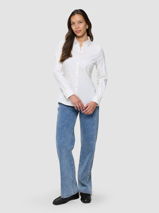 En kvinne iført en Women’s Oxford Shirt White Orchid Slim, som hun har stappet inn i lyseblå jeans og svarte loafers.