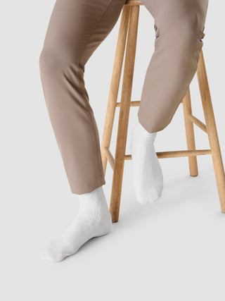 En person som har på seg «Socken 2er Pack White»-ribbestrikkede sokker med sømløs tå, sitter på en trekrakk.