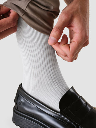 En person som tar på seg en ribbet sokk fra «Socken 2er Pack White», som er stappet inn i en svart skinnloafer.