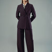 En kvinne har på seg en Women’s Avira Blazer i fargen Burgundy Berry, en hvit skjorte, et grått slips og matchende bukser med bredt ben og dobbeltspent.
