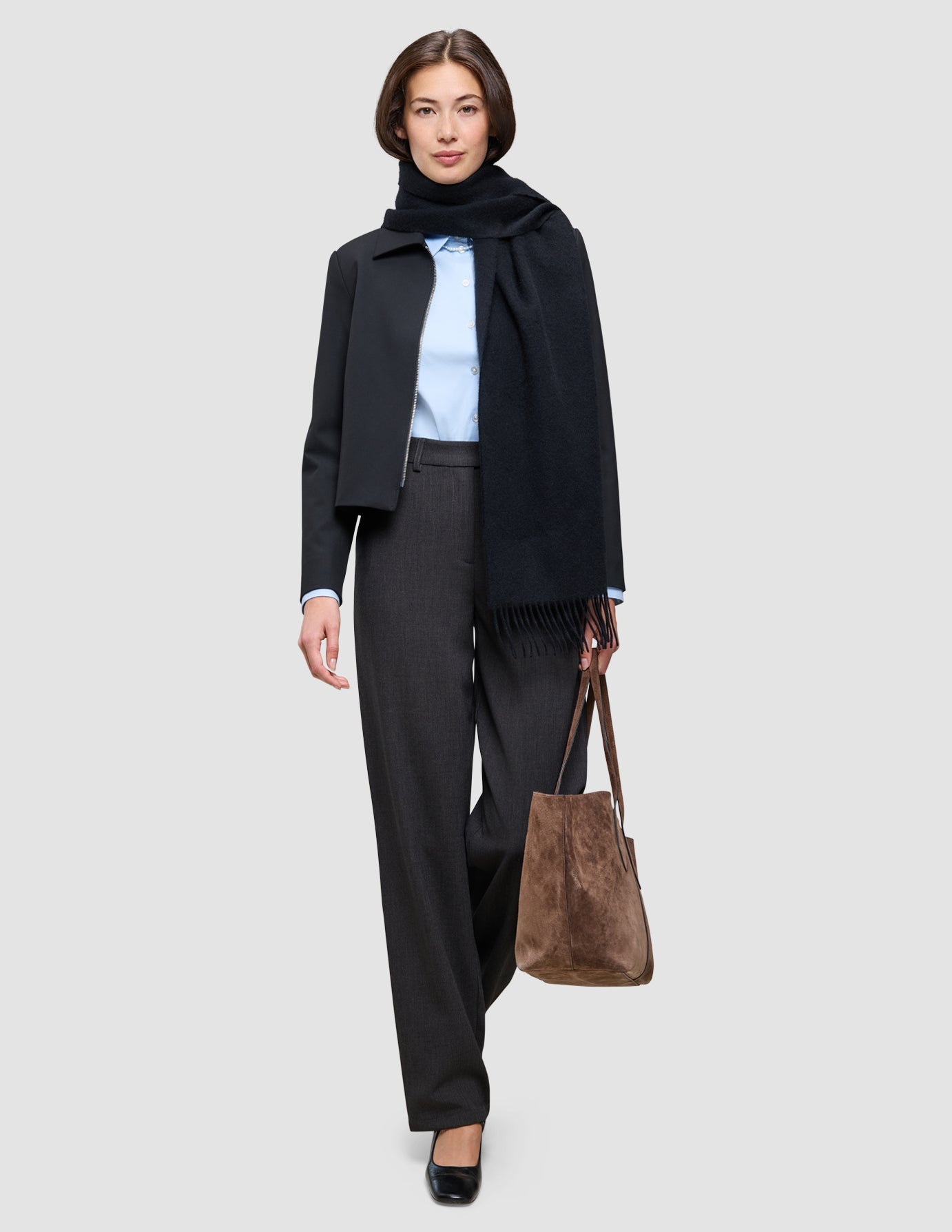 En kvinne har på seg et antrekk som gir et elegant kontorutseende: en lyseblå Oxford-skjorte, mørke bukser og et skjerf, og hun bærer en totebag.