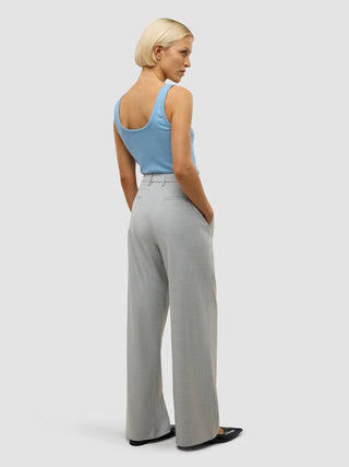 En person sett bakfra har på seg en blå tank-top og «Women’s Skye Pants Wide Grey Pine Melange», med hendene i lommene.