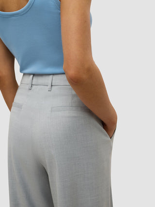 En person i en blå tank-top og «Women’s Skye Pants Wide Grey Pine Melange», med den ene hånden i lommen.