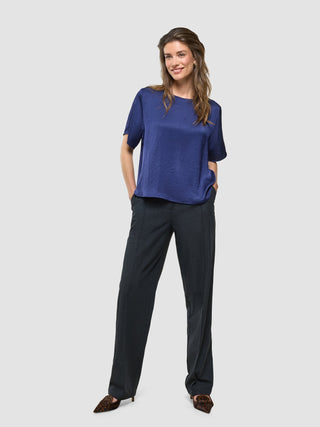 En kvinne iført en «Women’s Amara Blouse Navy» med krøllete tekstur, kombinert med mørke bukser og hendene i lommene.