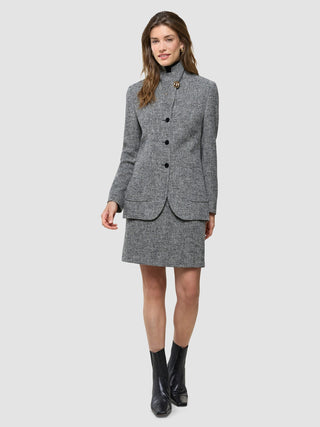 En kvinne som har på seg en «Ashryn Set Domino Herringbone»-blazer og kort skjørt, sammen med svarte ankelstøvler.