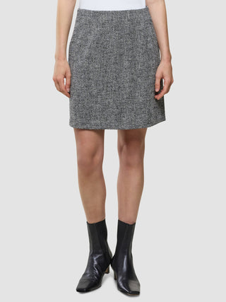 En person som har på seg et Ashryn Set Domino Herringbone-blazer og kort skjørt samt svarte ankelstøvler.