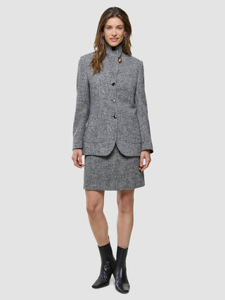 En kvinne har på seg en Ashryn Domino-blazer med fiskebeinmønster, et matchende skjørt og svarte ankelstøvler i skandinavisk design.