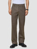 En person som har på seg mørkbeige Atelier Pants Relaxed-bukser i brutt twill og svarte skinnsko.