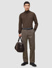 En mann i en brun genser med kvart glidelås og Atelier Pants Relaxed Dark Beige-bukser holder en mørk veske som fremhever skandinavisk design.