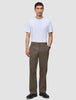 En mann har på seg en hvit T-skjorte, svarte sko og Atelier Pants Relaxed Dark Beige i brutt twill.