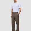 En mann har på seg en hvit T-skjorte, Atelier Pants Relaxed Dark Beige og svarte sko.
