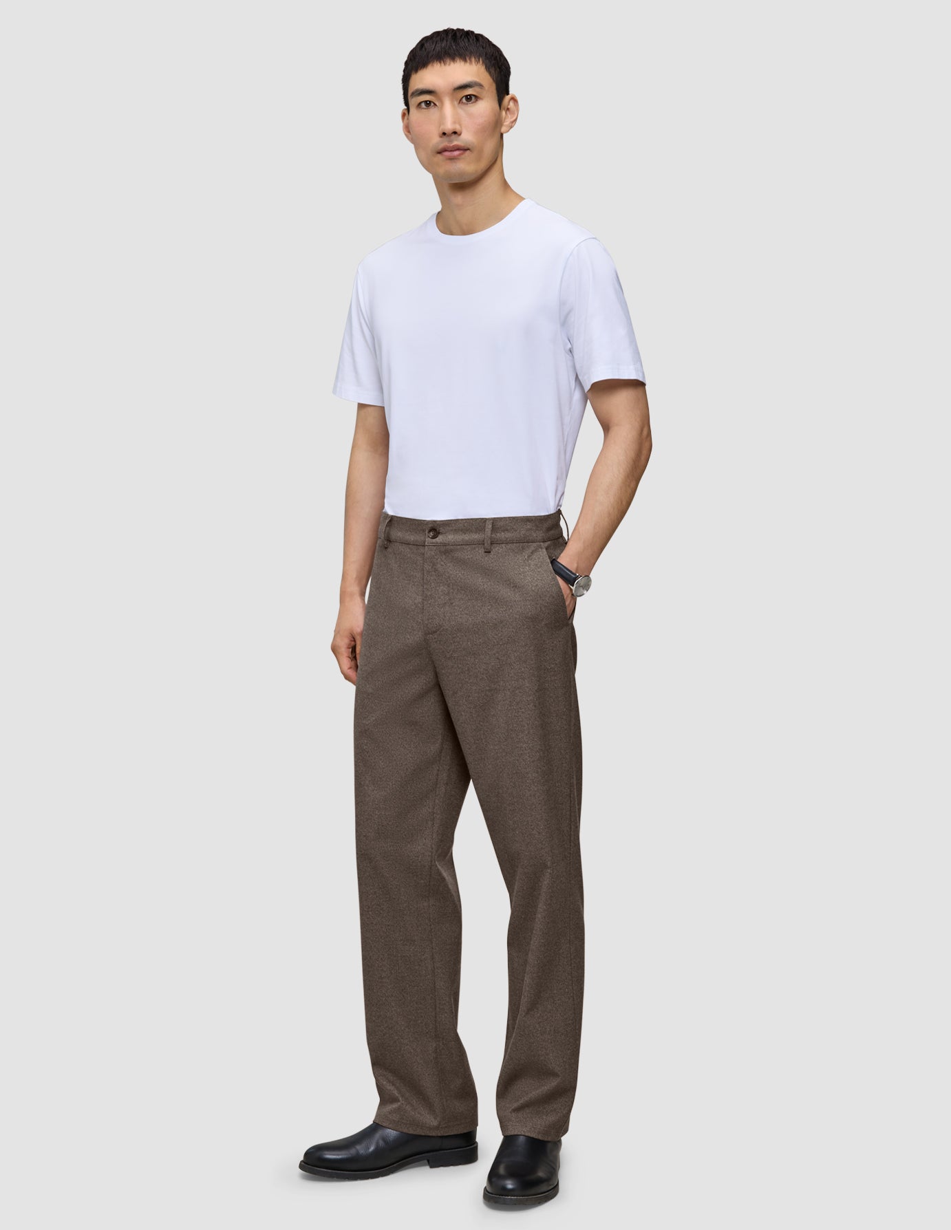 En mann har på seg en hvit T-skjorte, Atelier Pants Relaxed Dark Beige og svarte sko.
