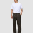 En mann i en hvit T-skjorte og Atelier Pants Relaxed Dark Brown, som gjenspeiler en stil preget av skandinavisk design.