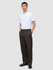 En mann i en hvit T-skjorte og mørkebrune Atelier Pants Relaxed, med hendene i lommene.