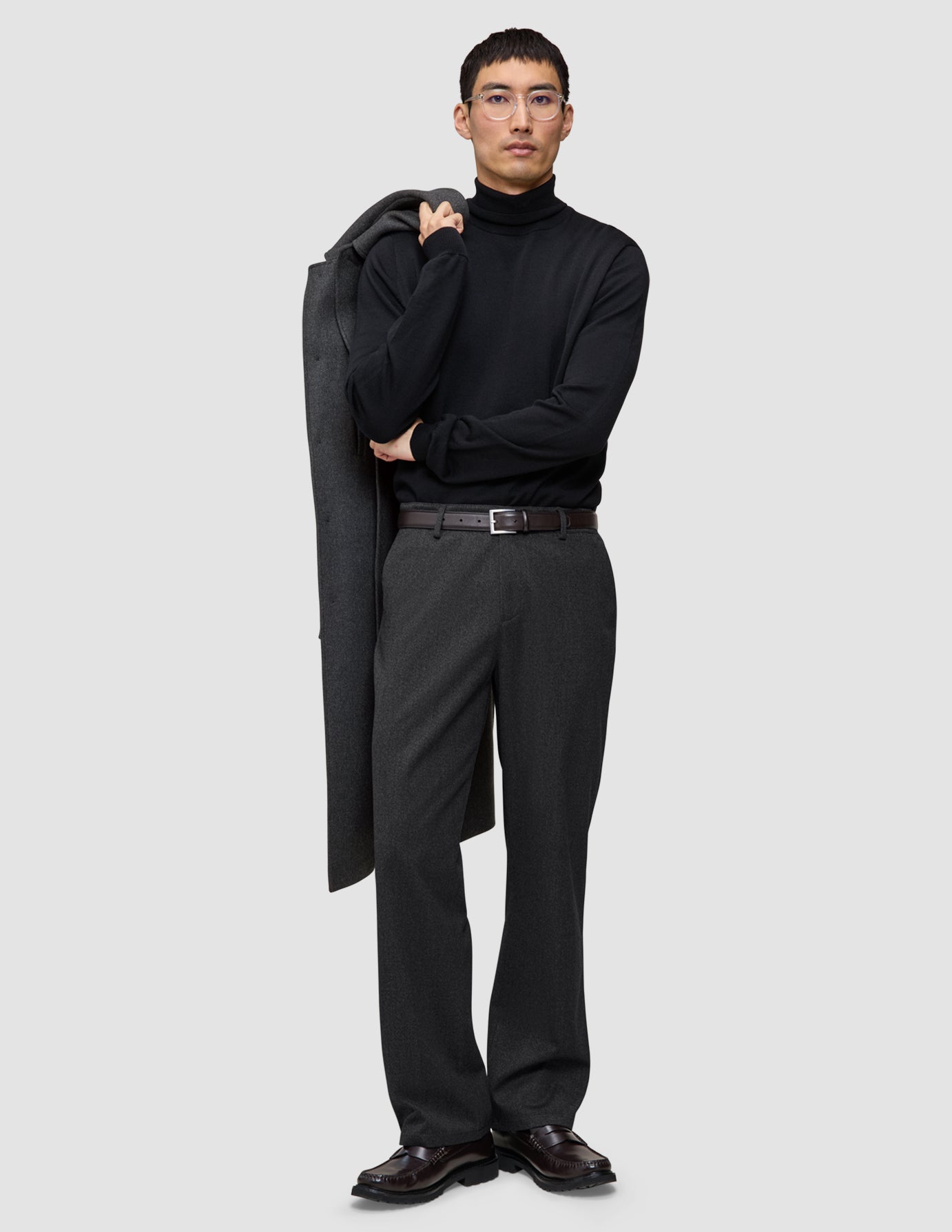 En mann i svart turtleneck og mørkegrå Atelier Pants Relaxed, som holder en frakk over skulderen på en avslappet måte.