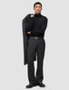 En mann i svart turtleneck og mørkegrå Atelier Pants Relaxed, som holder en frakk over skulderen på en avslappet måte.