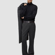 En mann i svart turtleneck og mørkegrå Atelier Pants Relaxed, som holder en frakk over skulderen på en avslappet måte.