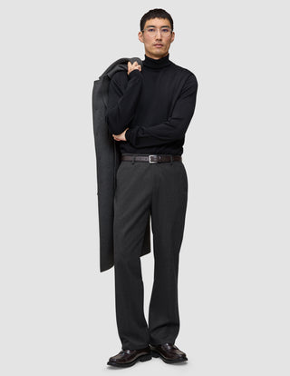 En mann i svart turtleneck og mørkegrå Atelier Pants Relaxed, som holder en frakk over skulderen på en avslappet måte.