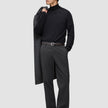 En mann i svart turtleneck og mørkegrå Atelier Pants Relaxed, med en jakke i skandinavisk design over skulderen.