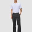 En mann i hvit T-skjorte, Atelier Pants Relaxed i mørkegrått og mørke loafers – et levende eksempel på skandinavisk design.