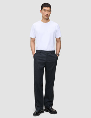 En mann i hvit T-skjorte, mørk marineblå Atelier Pants Relaxed og svarte loafers, som gjenspeiler det rene skandinaviske designet.