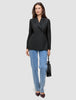 En kvinne har på seg en svart Women’s Avira Blazer Black, blå jeans og mørke høyhælte sko, mens hun holder en liten svart håndveske.
