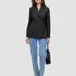 En kvinne har på seg en svart Women’s Avira Blazer Black, blå jeans og mørke høyhælte sko, mens hun holder en liten svart håndveske.