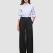En person som har på seg en hvit skjorte med knapper, stappet inn i et par Women’s Avira Pants Wide Black.