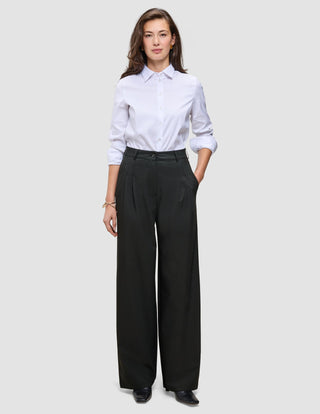 En person som har på seg en hvit skjorte med knapper, stappet inn i et par Women’s Avira Pants Wide Black.