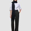 En kvinne har på seg en hvit skjorte med knapper, lange, svarte Women’s Avira Pants Wide Black-bukser og et langt, svart skjerf.