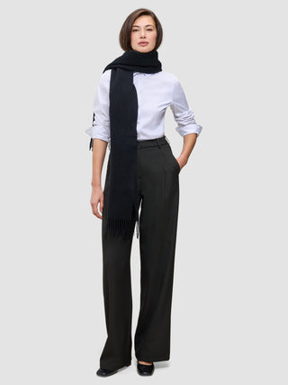 En kvinne har på seg en hvit skjorte med knapper, lange, svarte Women’s Avira Pants Wide Black-bukser og et langt, svart skjerf.