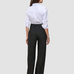 En kvinne sett bakfra, iført en hvit skjorte med knapper og svarte Women’s Avira Pants Wide Black-bukser med høy midje.