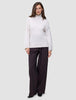 En kvinne kledd i en Women’s Chunky Soft Wool Knit Turtleneck Sugar Melange og mørke bukser med vide ben.