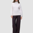 En kvinne kledd i en Women’s Chunky Soft Wool Knit Turtleneck Sugar Melange og mørke bukser med vide ben.