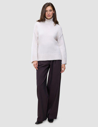 En kvinne kledd i en Women’s Chunky Soft Wool Knit Turtleneck Sugar Melange og mørke bukser med vide ben.